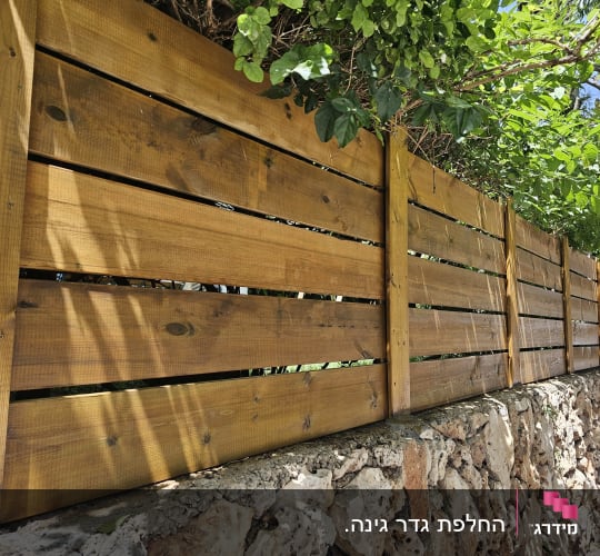 גדר עץ על קיר אבן עם צמחייה ירוקה